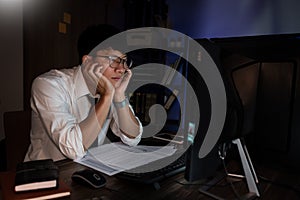 Stressed Young asian business man working late night alone in office late his eyes are gonna closing at table and looking headache