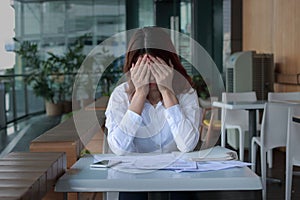 Stressed young Asian business woman covering face with hands on the desk in office