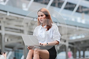 Stressed young Asian business woman using laptop for job at outside office.