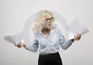 Stressed young businesswoman with papers feeling angry or having nervous breakdown, standing over light background