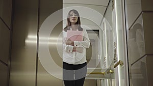 Stressed young businesswoman standing in lift with documents and elevator door closes. Portrait of embarrassed beautiful