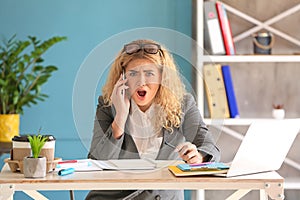 Stressed young businesswoman talking on phone in office