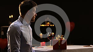 Stressed young man blowing out candles and leaving present on table, going away