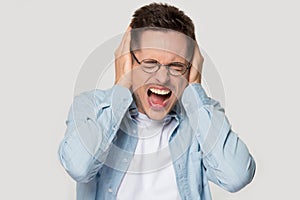Stressed young man in eyeglasses annoyed by loud sound.