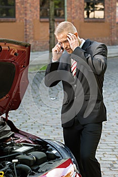 Stressed young man with his breakdown car calling on cellphone