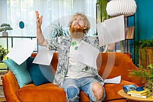 Stressed young man looking at unpaid bank debt loan, doing paperwork, planning budget, throws bills