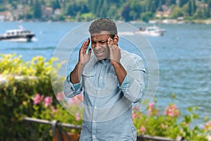 Stressed young man suffering from terrible headache standing outdoors.