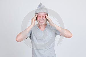 Stressed young man with tinfoil hat as conspiracy theory concept having headache