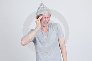 Stressed young man with tinfoil hat as conspiracy theory concept having headache