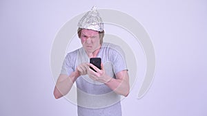Stressed young man with tinfoil hat using phone and looking scared