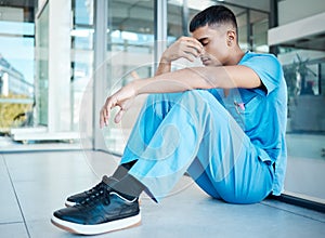 Stressed young medical professional sitting on the floor in his scrubs. A young nurse experiencing a painful headache