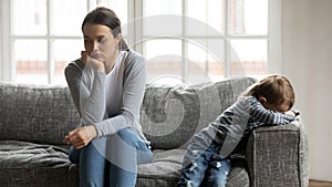 Stressed young mommy sitting separate on couch with offended son. photo