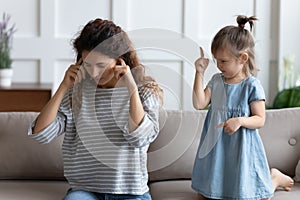 Stressed young mother covering ears, annoyed by bad daughters behavior.