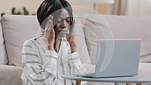 Stressed young tired woman freelancer businesswoman working remote on laptop at home holding on head feeling pain