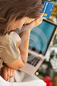 Stressed young woman with credit card and laptop in front of christmas tree