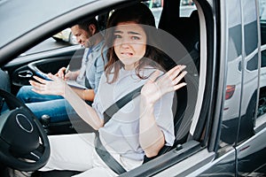 Stressed young woman on driver`s seat of black car throws up her hands in confusion and bites her lip. Upset driving