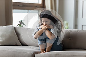 Stressed young woman embracing knees, sitting alone on couch.