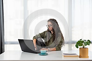 Stressed young woman holding head in hands and feeling demotivated while sitting at her home office and working remotely on laptop