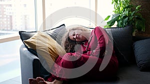 Stressed young woman lying on sofa, embracing belly, suffering from stomachache. Unhappy 20s girl having menstrual