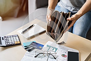 Stressed young woman open her empty wallet and calculating expenses