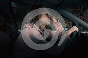 Traffic accident. Stressed woman is sitting behind the wheel of car and holding her head in despair, covering her eyes