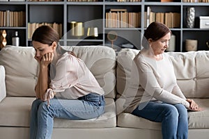 Stressed young woman sitting separately with offended mature mother.