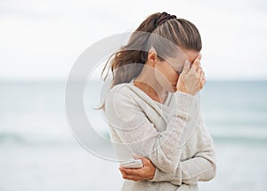 Stressed young woman in sweater on beach with cell phone