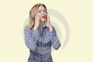 Stressed young woman touching her face while standing on white background.