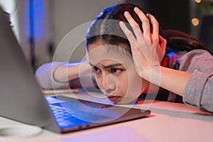 Stressful Asian business woman sitting on the chair and looking on the laptop screen on office at night