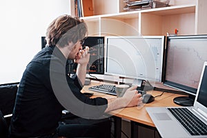 Stressful day at the office. Young businessman holding hands on his face while sitting at the desk in creative office
