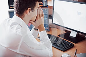 Stressful day at the office. Young businessman holding hands on his face while sitting at the desk in creative office