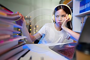 Stressful young Asian woman wearing headset and sitting on the chair with a pile of papers document on the table.