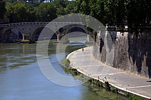 Stretch of river with bridge and embankment, on a sunny day, with an incidental unrecognizable person