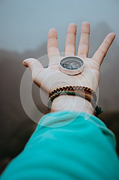 Stretched man arm with compass on the palm of the hand directed to mountain peaks on cloudy day