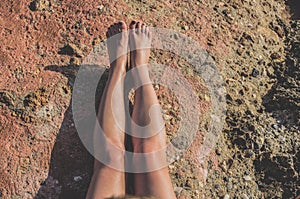 Stretched naked legs of a tanning woman sitting on the rocks