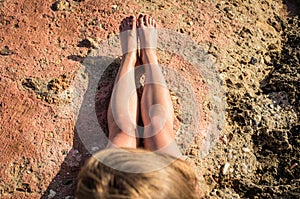 Stretched naked legs of a tanning woman sitting on the rocks