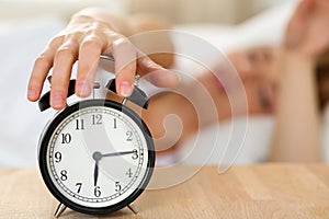 Stretching hand of sleepy young woman trying kill alarm clock
