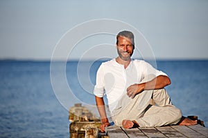 Stretching his muscles to stay flexible. Portrait of a handsome mature man doing yoga on a pier out on the ocean.