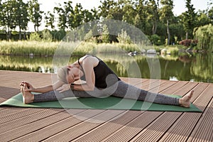 Stretching legs. Full length of a young beautiful fitness woman in sportswear doing twine exercise on yoga mat in park