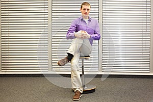 Stretching legs in office - man sitting on pneumatic stool exercising