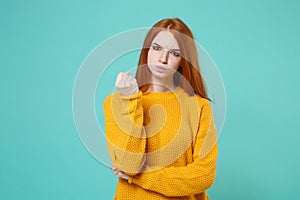 Strict angry young redhead woman girl in yellow sweater posing isolated on blue turquoise background studio portrait