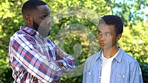 Strict black dad looking at guilty teenage son, upbringing methods, family