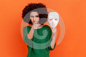 Strict bossy woman with Afro hairstyle in green casual style sweater holding white mask in hand