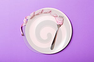 Strict diet concept with empty space fro your design. Top view of plate with fork in measuring tape on purple background photo