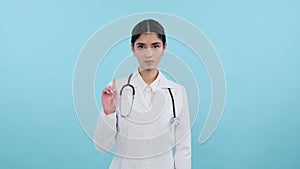 Strict female doctor shakes her finger on blue background