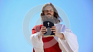 Strict God holding Bible against blue sky, reminding of faith and repentance