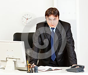 Strict modern businessman standing at office desk