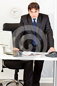 Strict modern businessman standing at office desk