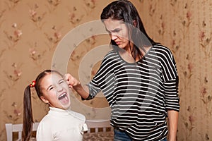 Strict mother holds her daughter by an ear.