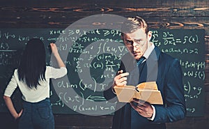 Strict teacher in glasses giving explanations while holding book. Tutor helping his young female student with math